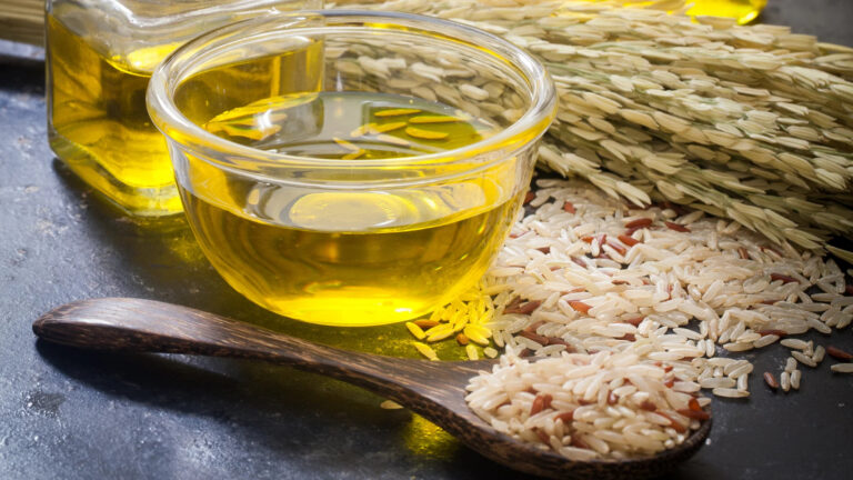 Edible oil in a glass bowl beside rice grains